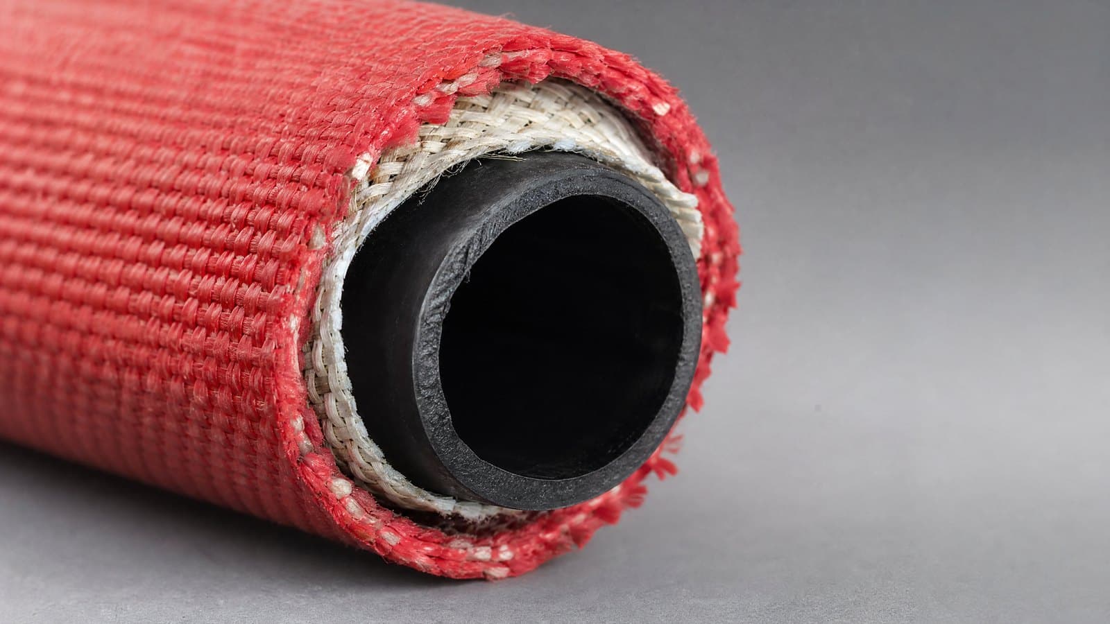Cut end of a red double-jacket fire hose showing outer red jacket, inner white jacket and black rubber liner