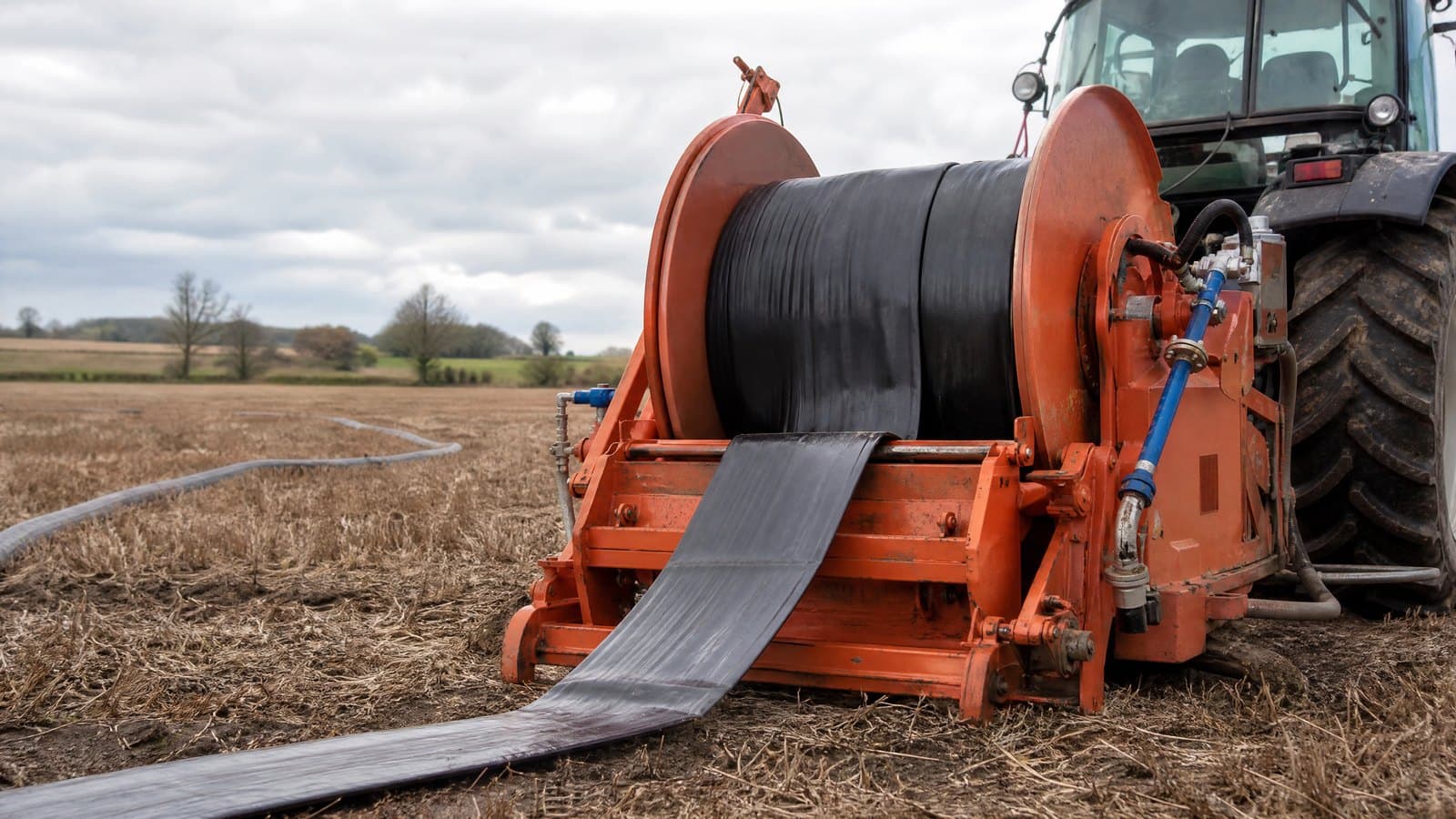 Tractor-mounted reel winding a black lay flat hose in across a harvested field