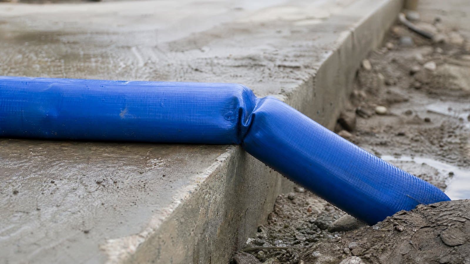 Pressurised blue lay flat hose kinked sharply over a concrete kerb edge