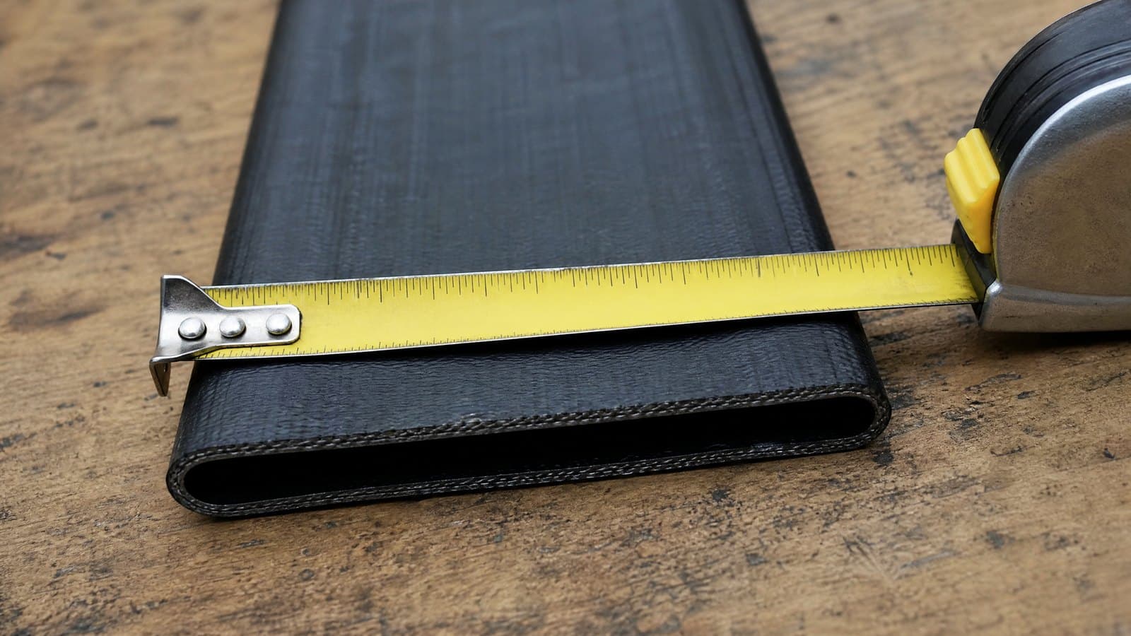 Tape measure laid across a flattened black lay flat hose on a workbench to read its flat width