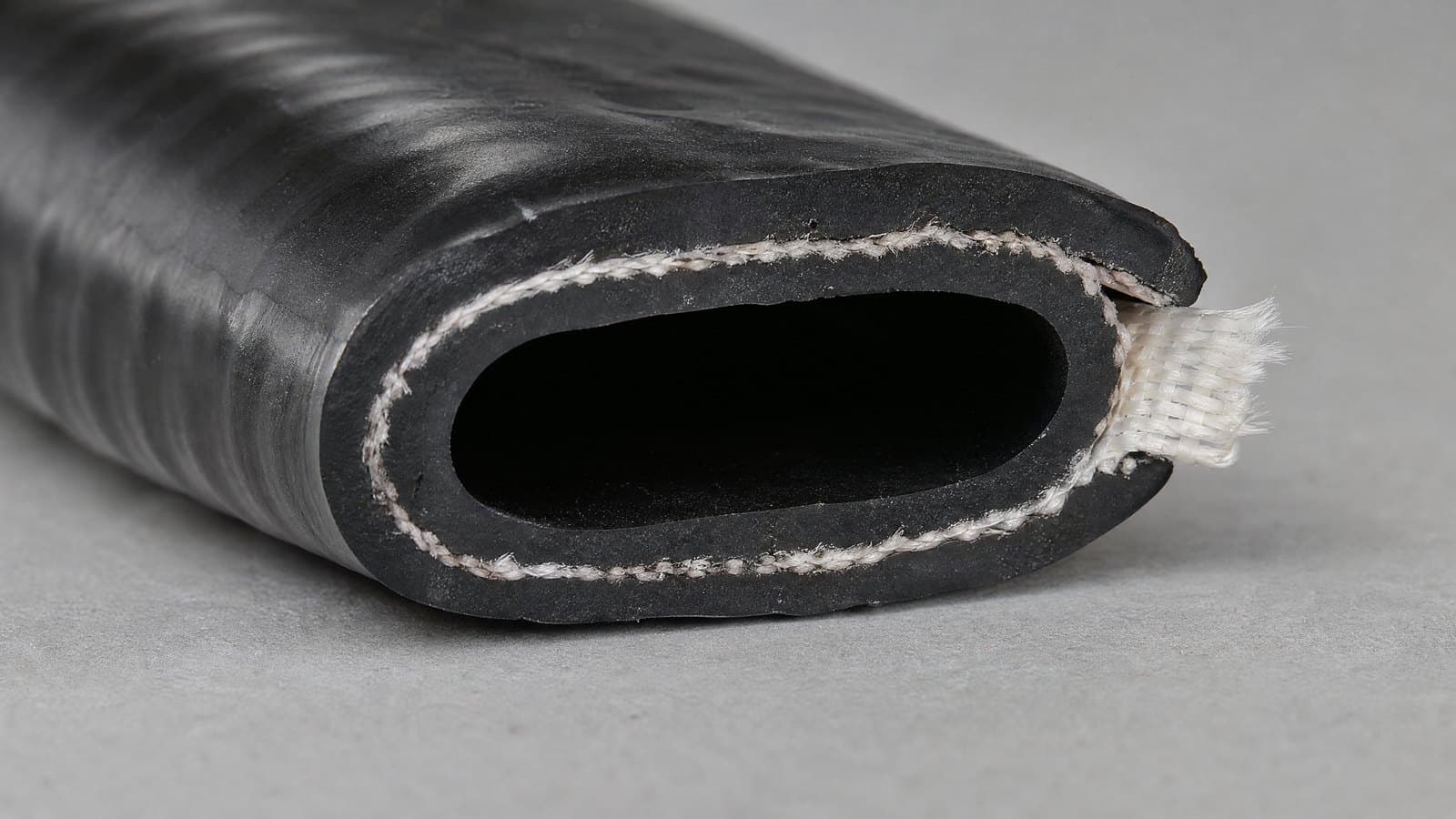 Cut end of a black TPU lay flat hose showing the white woven polyester jacket inside the wall
