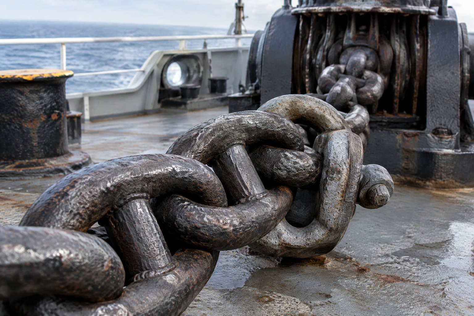 Heavy stud link anchor chain on a ship's foredeck, each link with a stud across its middle, the windlass behind