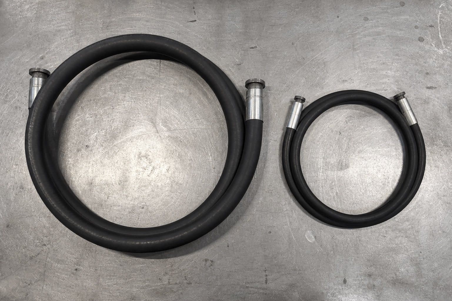 Two hoses of the same bore coiled side by side — standard braid making a wide loop, compact hose a visibly tighter one