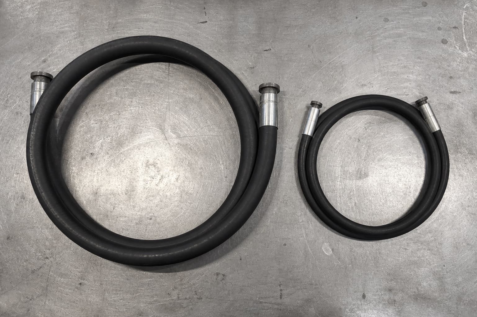 Two hoses of the same bore coiled side by side — standard braid making a wide loop, compact hose a visibly tighter one