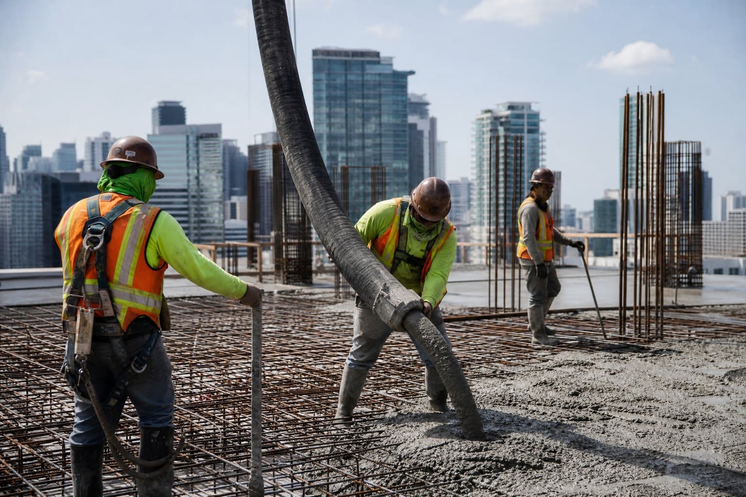 Workers on a high-rise slab guiding the flexible end hose of a concrete pump to place concrete into steel reinforcement
