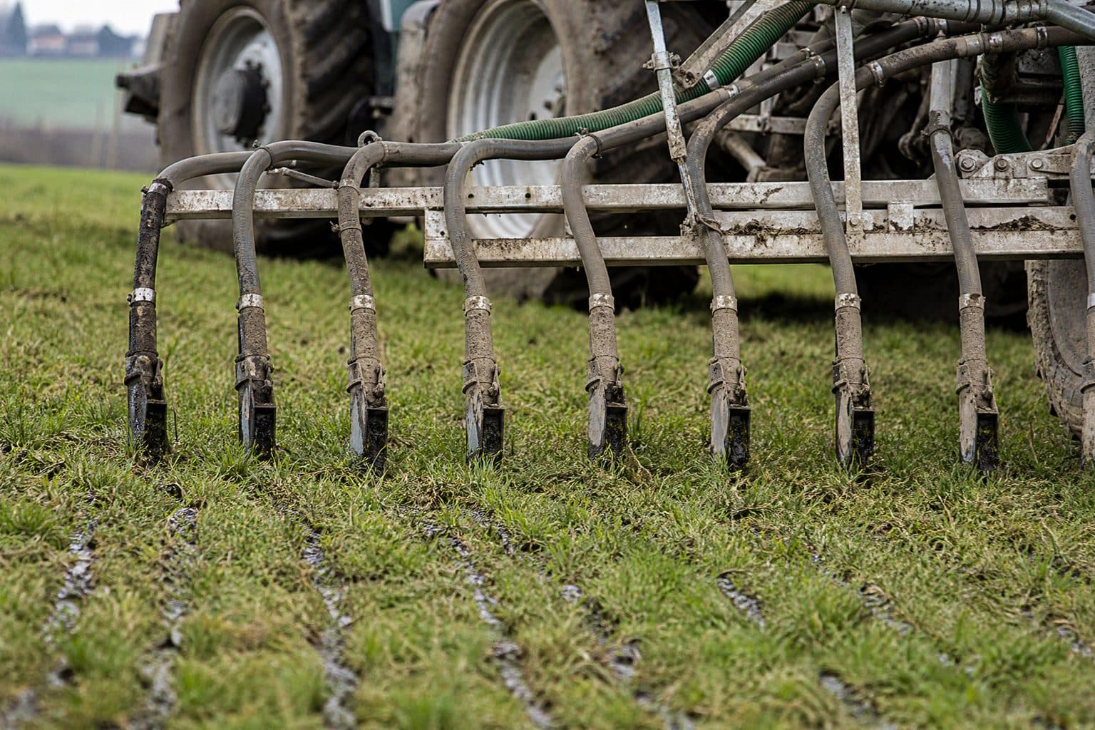 Trailing-shoe slurry applicator placing slurry in narrow bands at the base of grass, tractor wheels behind