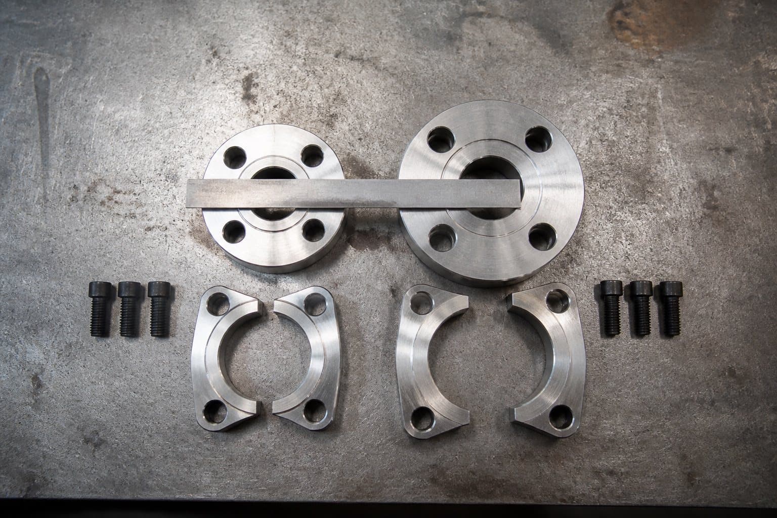 Two four-bolt split flange heads of the same bore side by side, one visibly thicker with wider bolt spacing, a steel rule across both