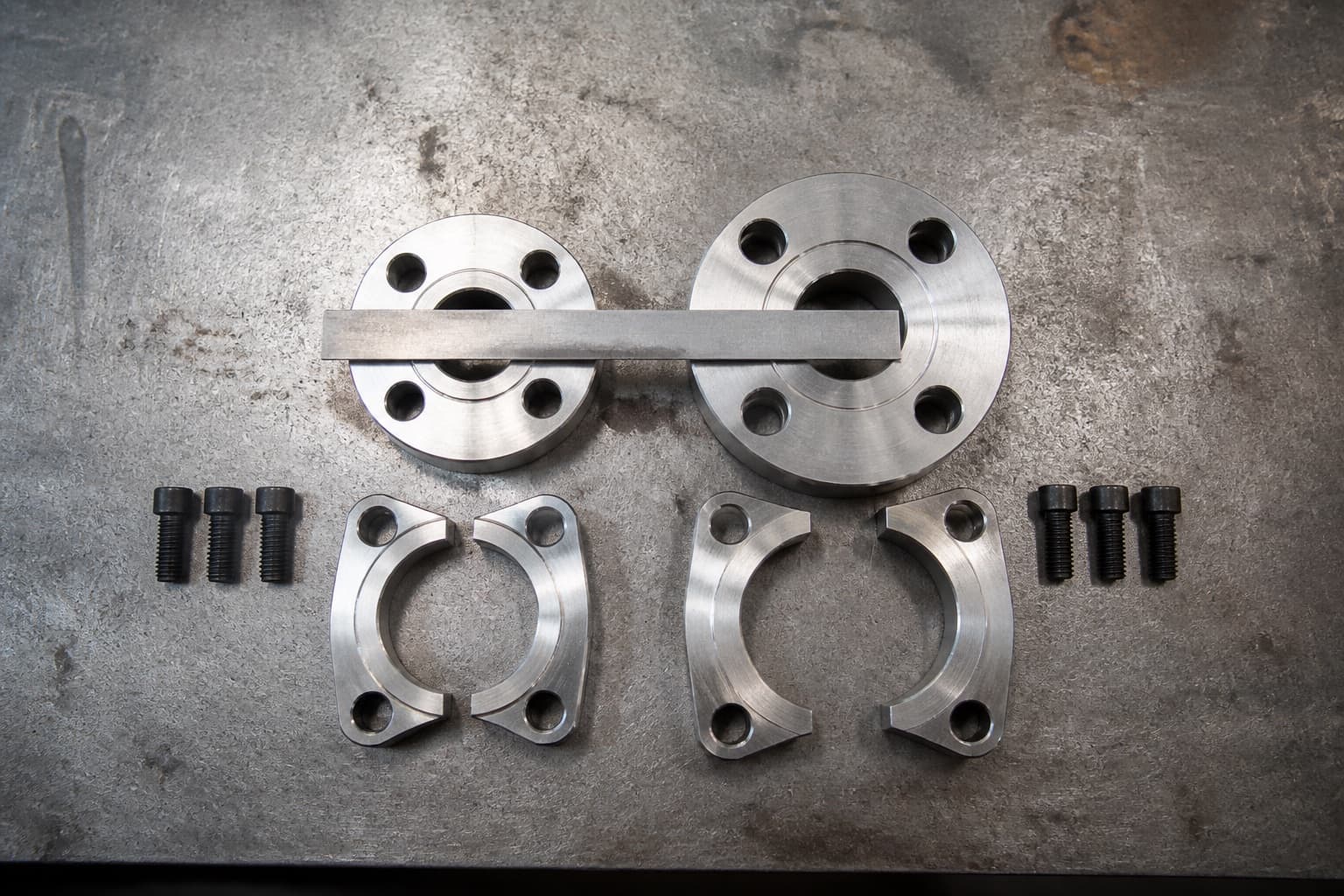 Two four-bolt split flange heads of the same bore side by side, one visibly thicker with wider bolt spacing, a steel rule across both