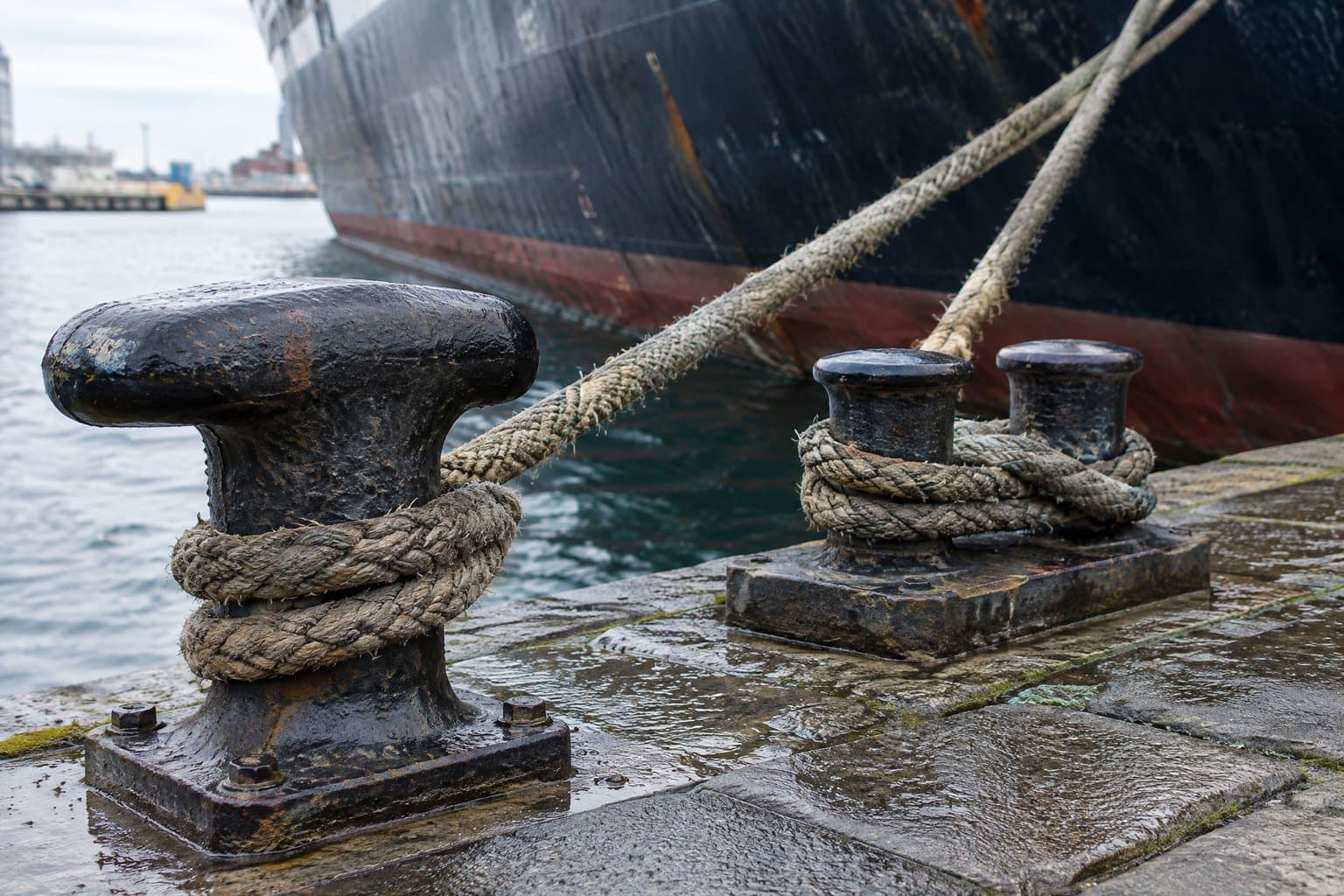 Mooring ropes on a T-head bollard and double bitts on a quay beside a moored ship
