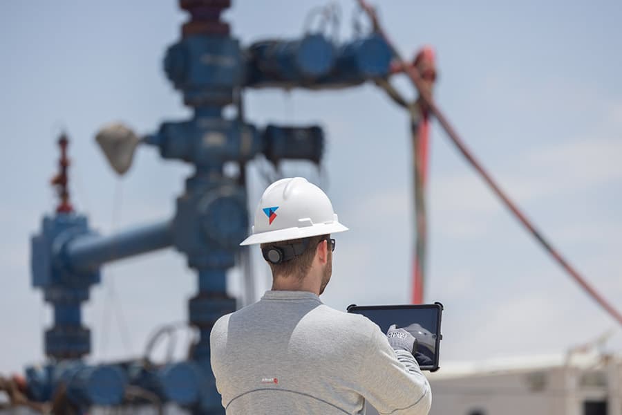 Engineer with a tablet beside a blue frac tree on a wellsite